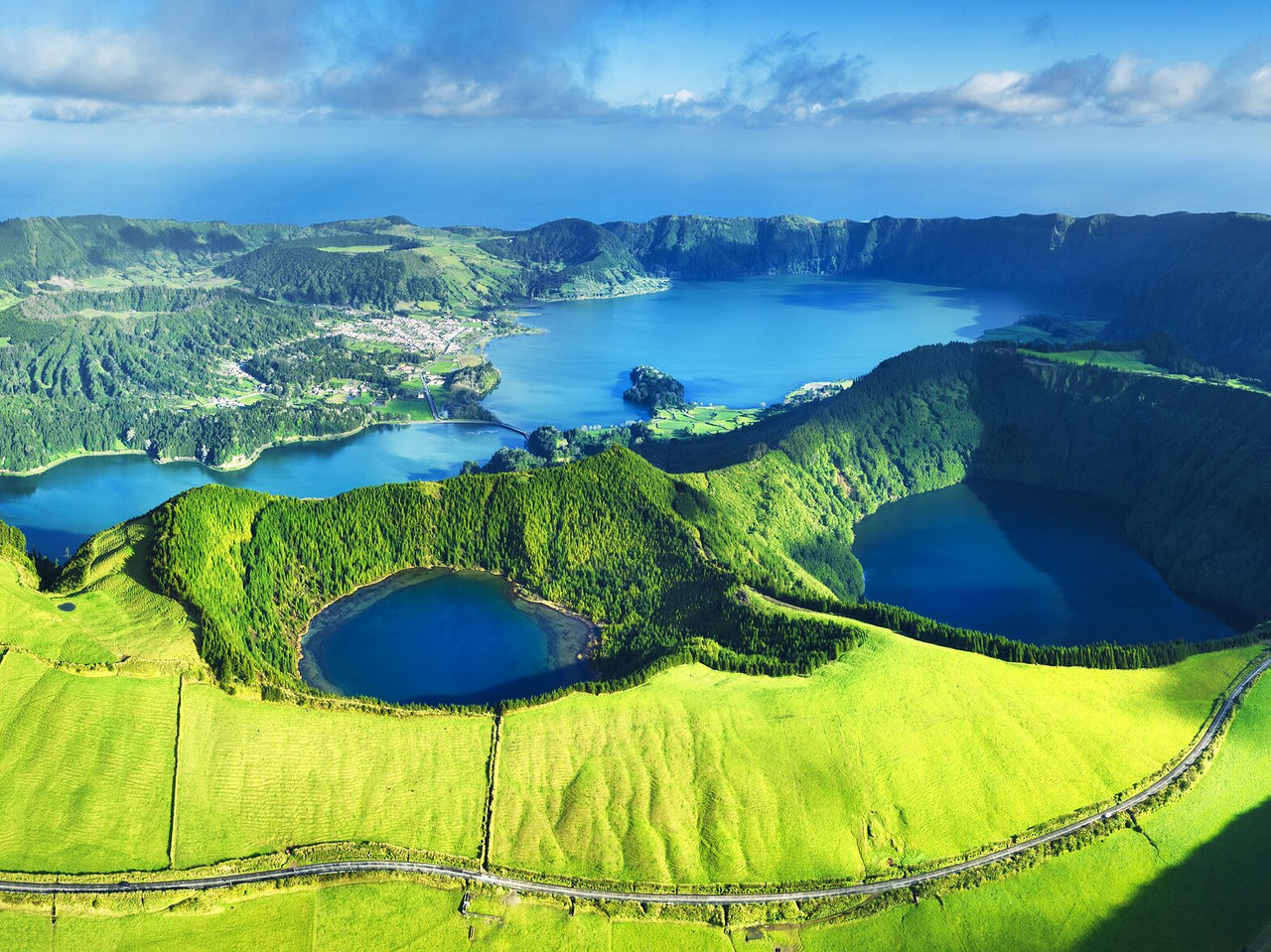 Explore Hotels in the Azores with an aerial view of volcanic lakes, green hills and coastal cliffs below