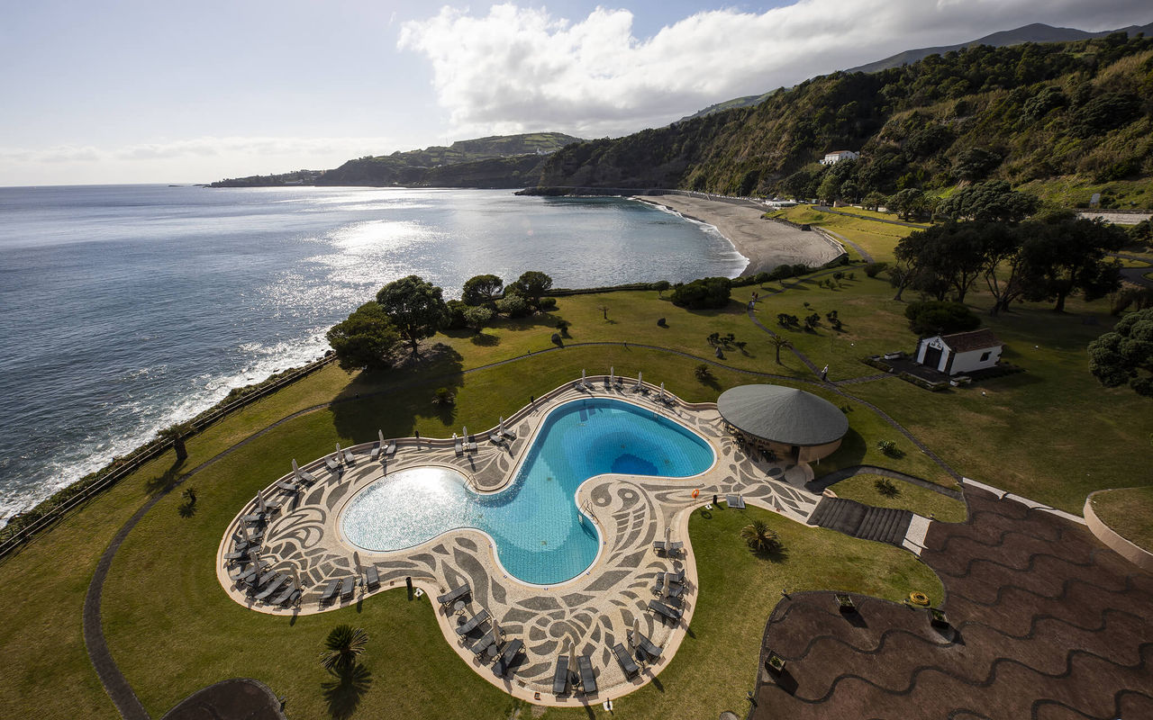 Pool of a resort in São Miguel, Azores, surrounded by green gardens, with sun loungers and a view of a hillside