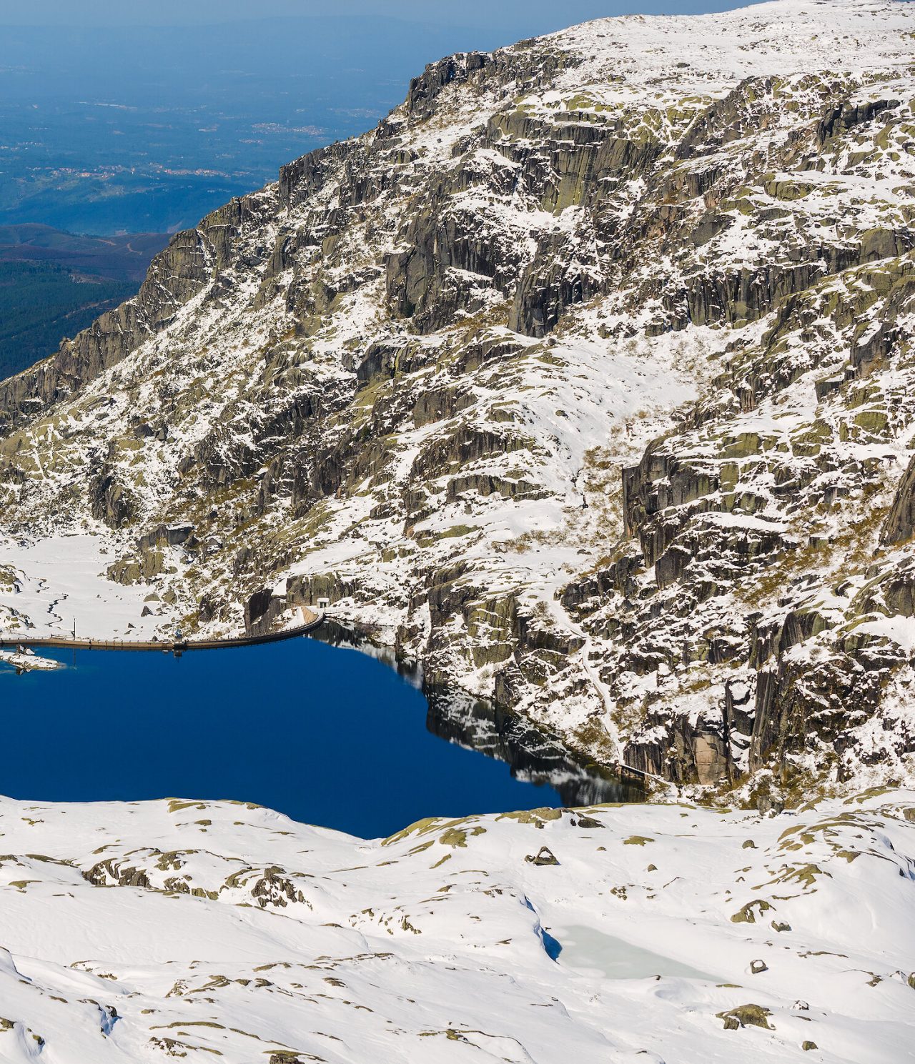 Explore Hotels in Central Portugal featuring snowy cliffs descending toward a deep blue mountain lake