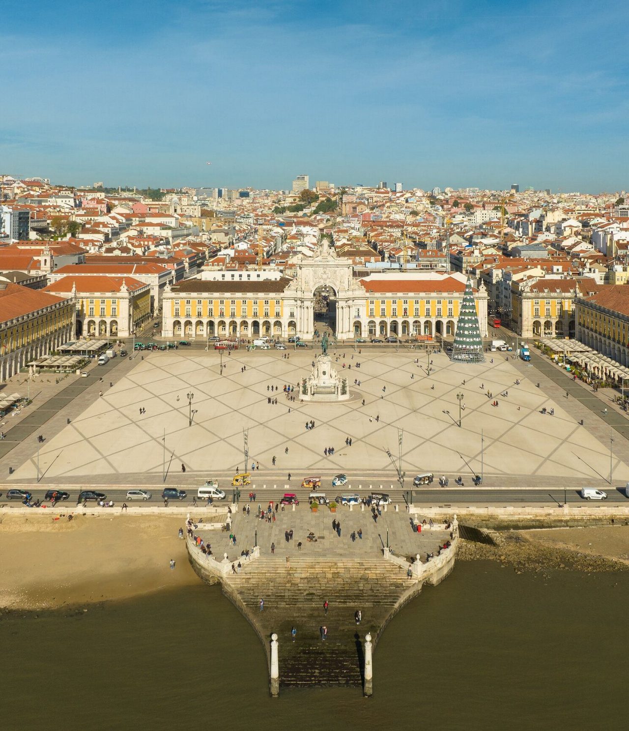 Aerial view of Praça do Comércio in Lisbon, with the Tagus River in front, statue in the middle, and a Christmas tree