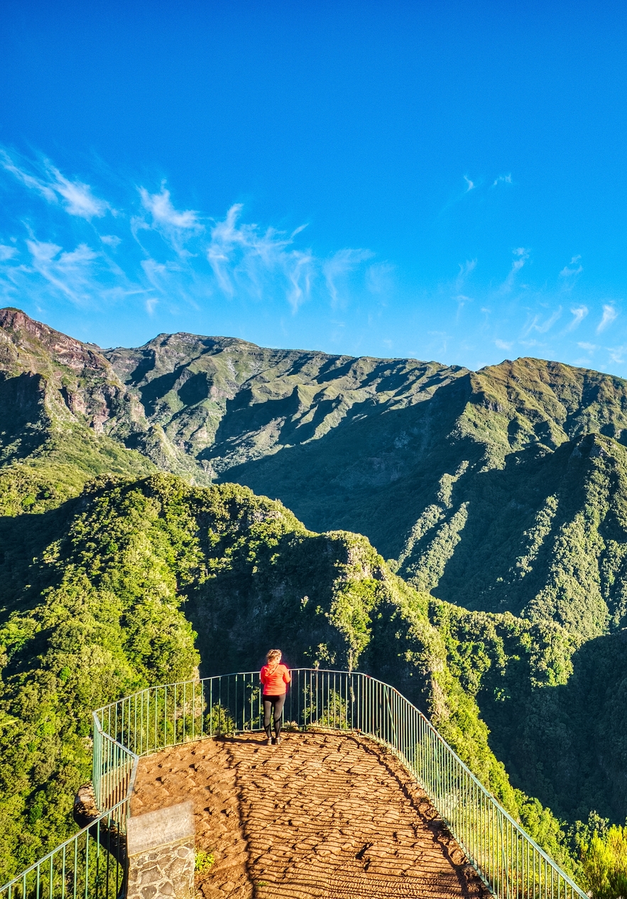 Person walking who stopped to enjoy the lush mountainous landscape at a viewpoint in Madeira