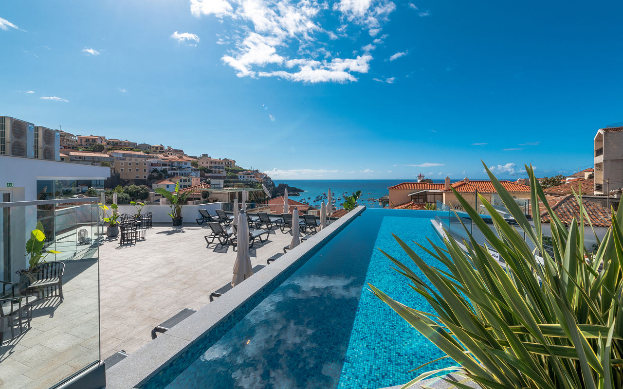 View of the outdoor pool and terrace of the hotel in Câmara de Lobos, Madeira, with the sea and city in the background
