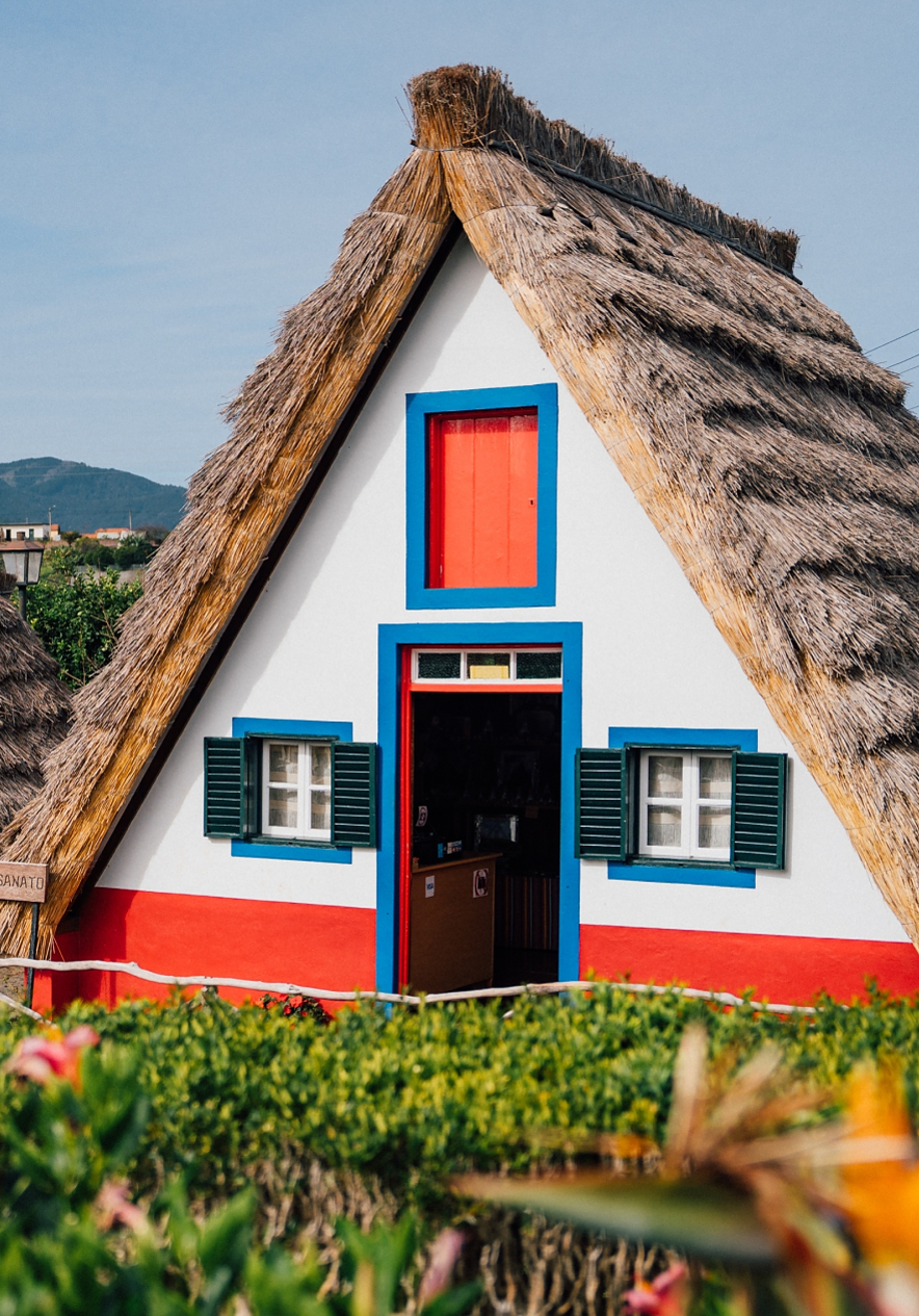 Two traditional houses with thatched roofs painted white with red and blue details in Funchal