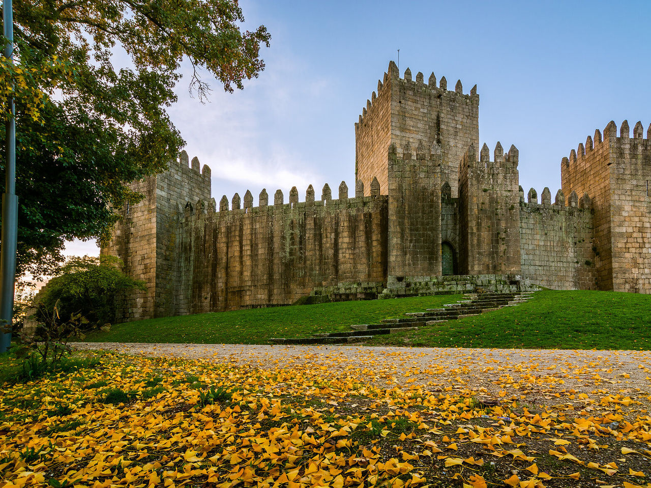 Guimarães Castle characterized by medieval architecture, surrounded by grass and fallen yellow leaves