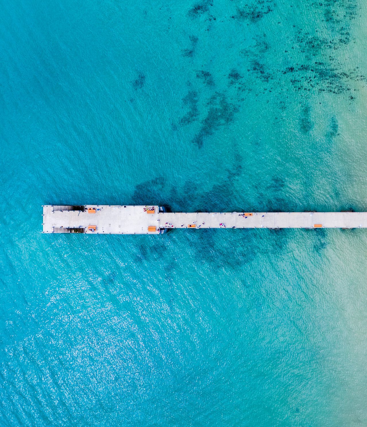 Aerial view of a cement pier, surrounded by turquoise blue sea, with stairs to descend to the water