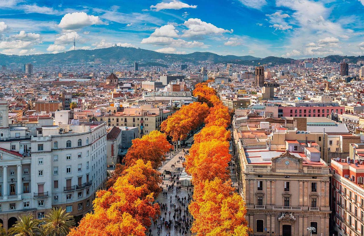 Aerial view over the city of Barcelona, with people strolling, colorful autumn trees, and various buildings