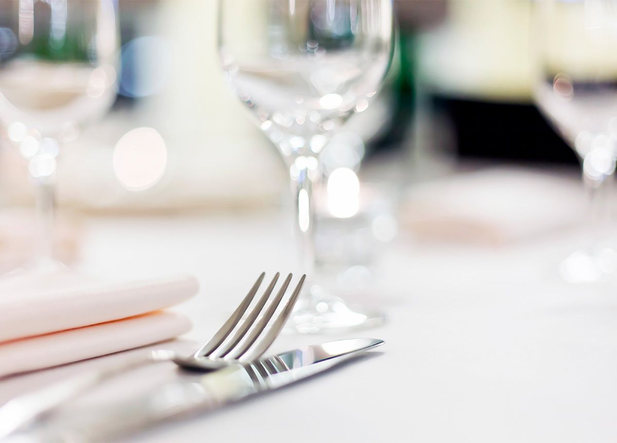 Elegantly set table with silver cutlery, cloth napkin, and glassware, in a well-lit setting