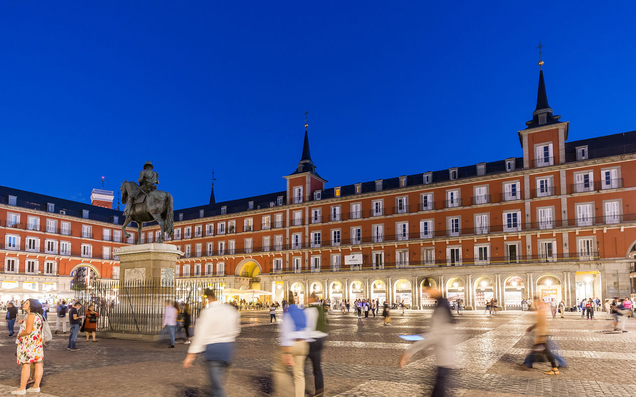 Explore Hotels in Madrid featuring Plaza Mayor at dusk with illuminated arcades and visitors crossing the square