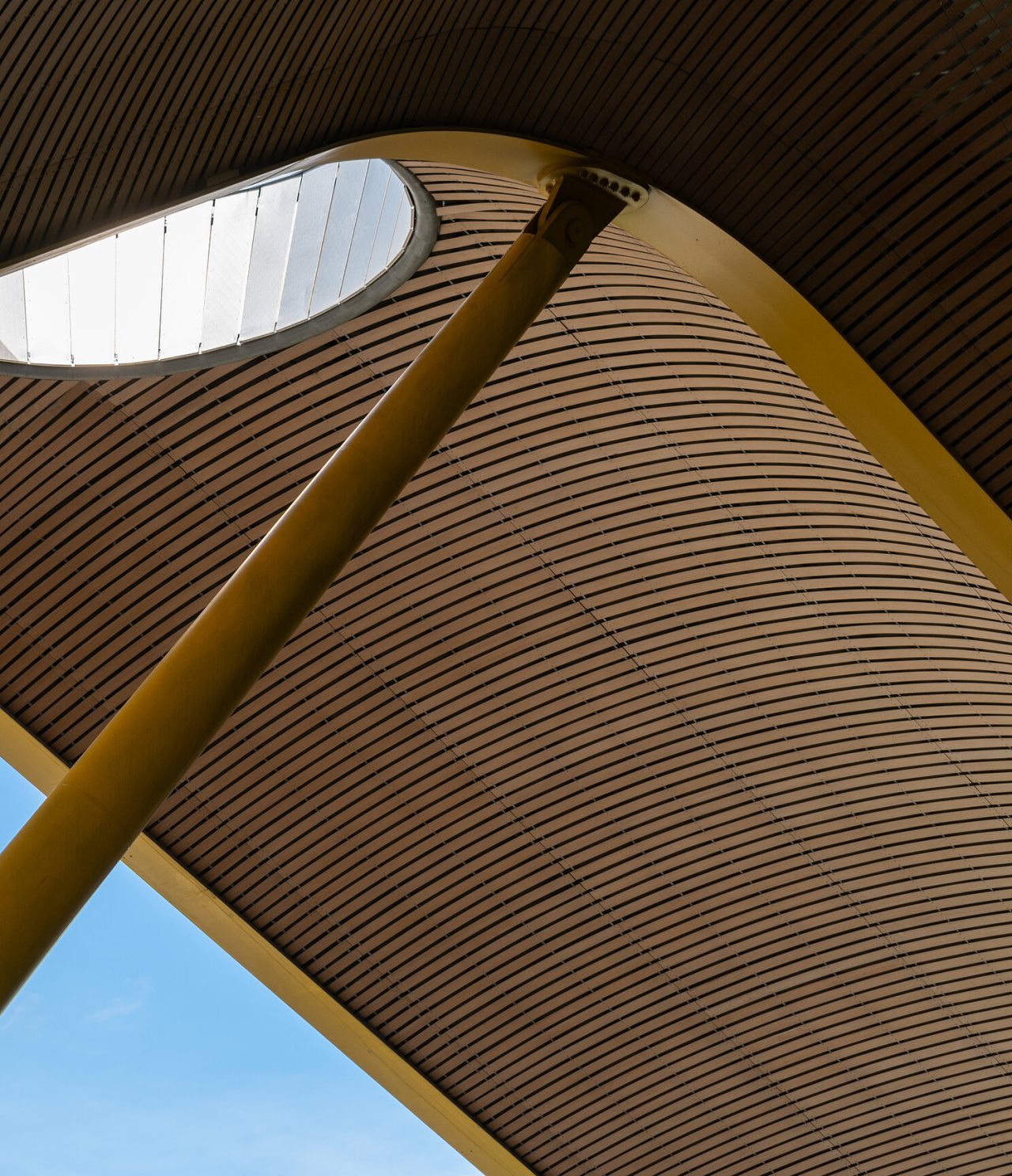 Explore Hotels in Madrid featuring a curved wooden canopy with skylight and tall yellow columns above blue sky