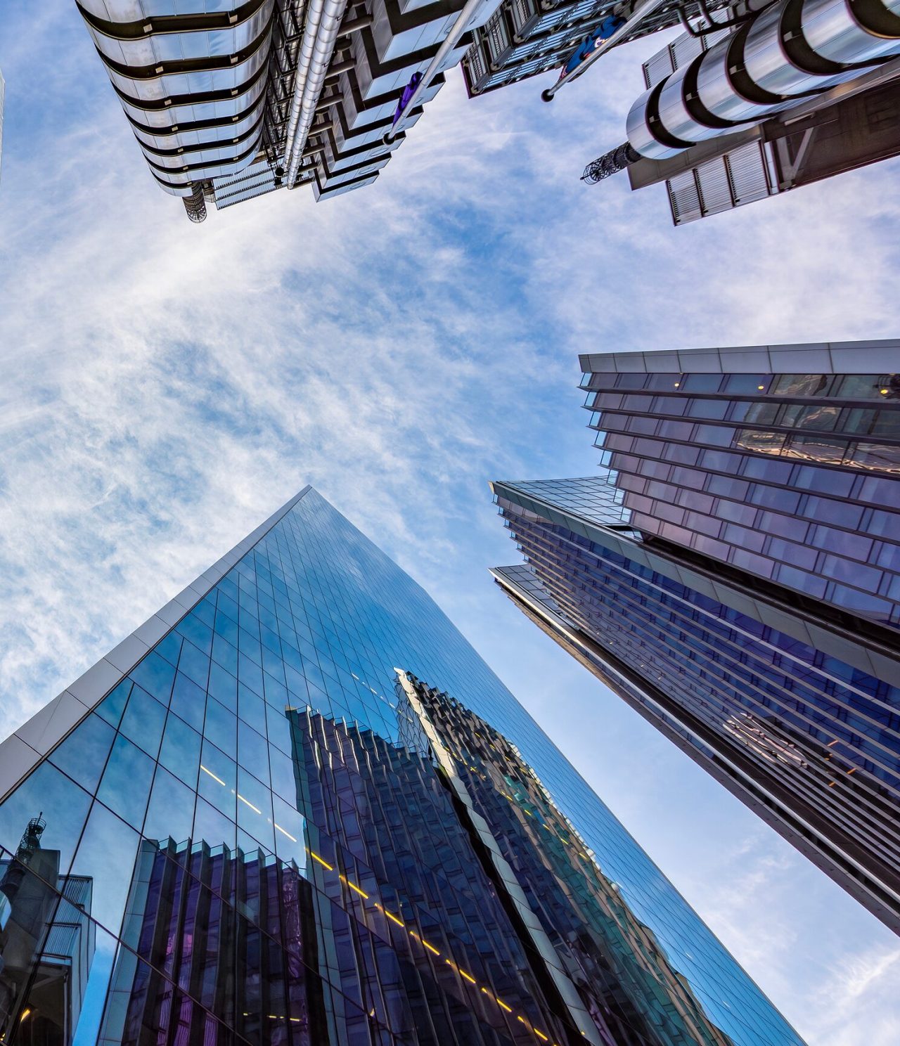 Explore Hotels in London featuring towering glass skyscrapers rising around a bright blue city sky