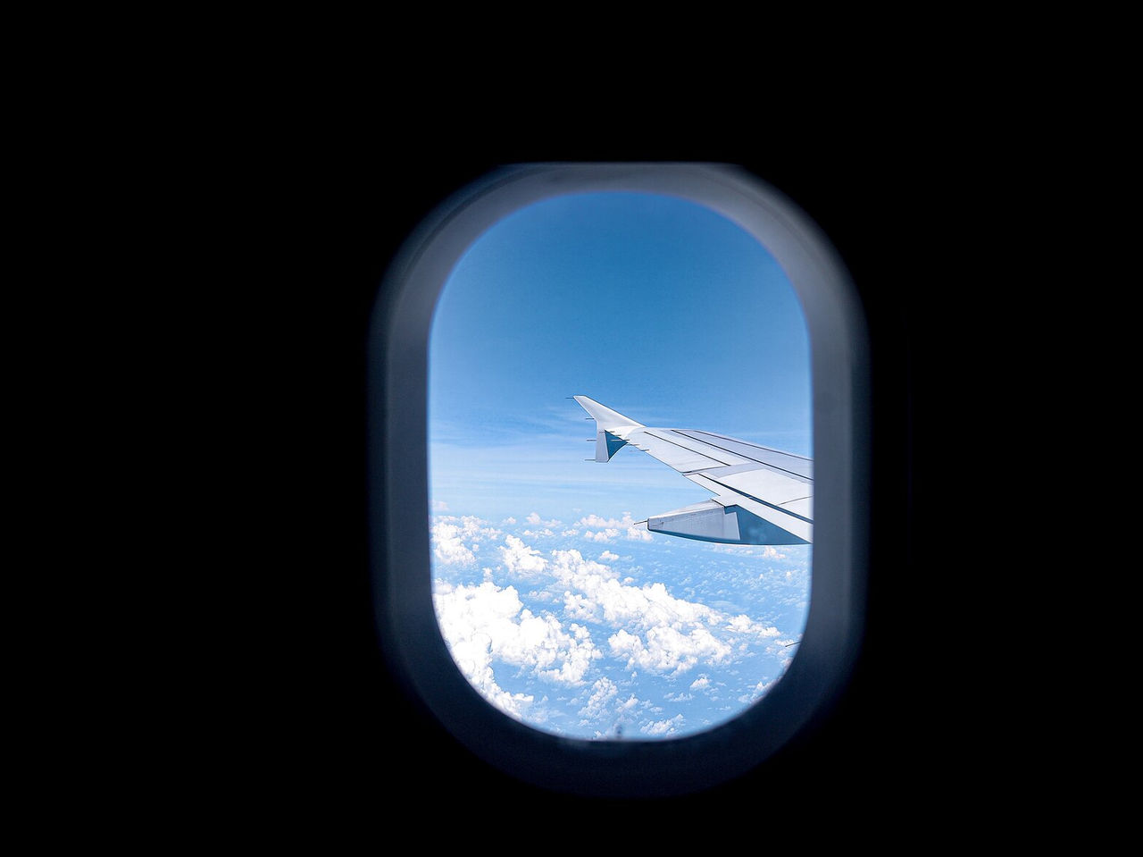 View from an airplane window, the wing, blue sky, and some clouds, heading to London