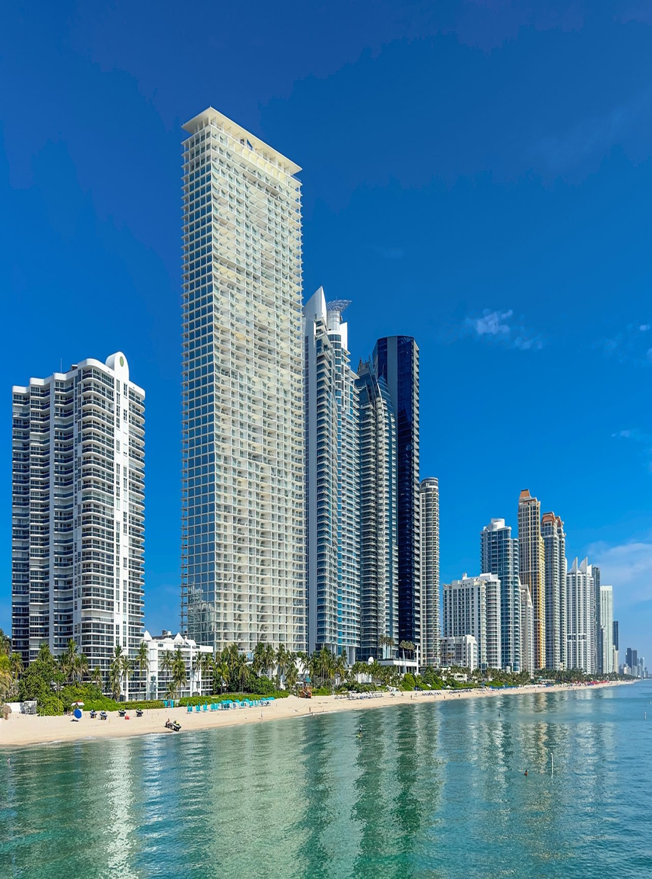 View over the coastline of Miami Beach with modern skyscrapers by the sea, light sandy beaches, and crystal blue water