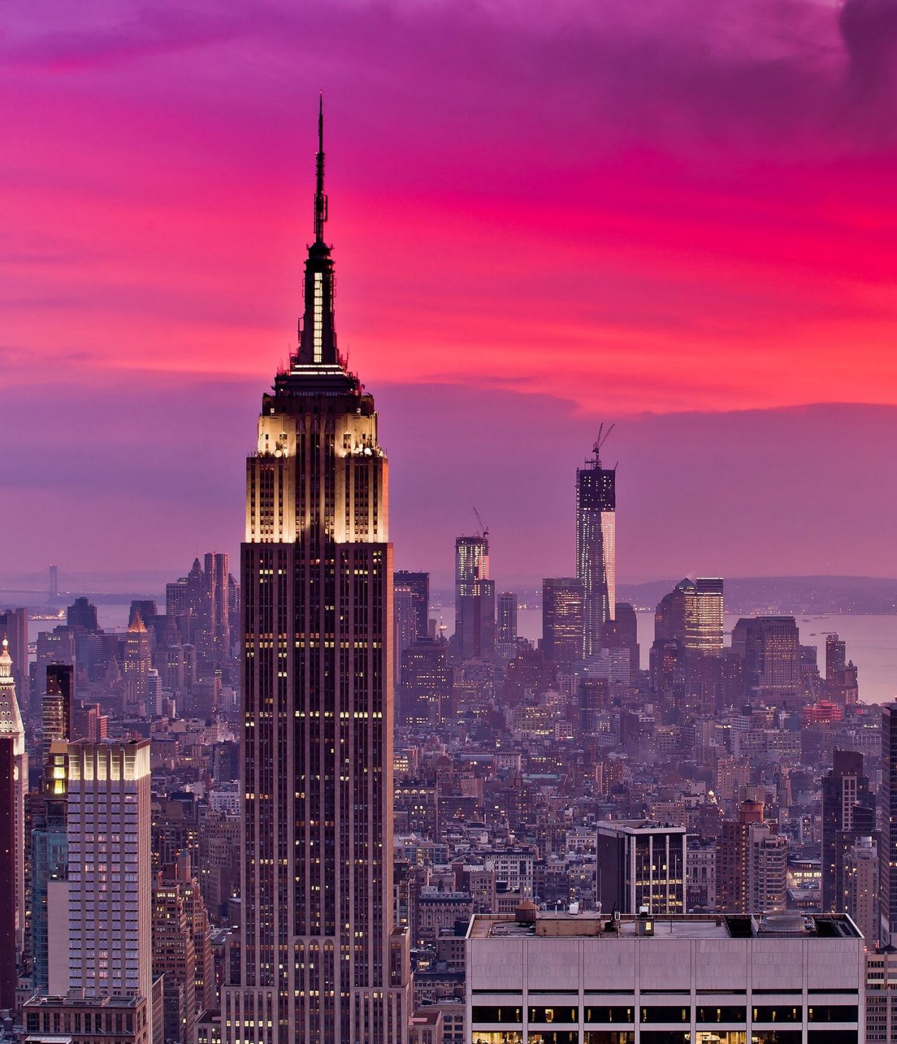 Aerial view of New York City, with the illuminated Empire State Building, surrounded by other skyscrapers and a river