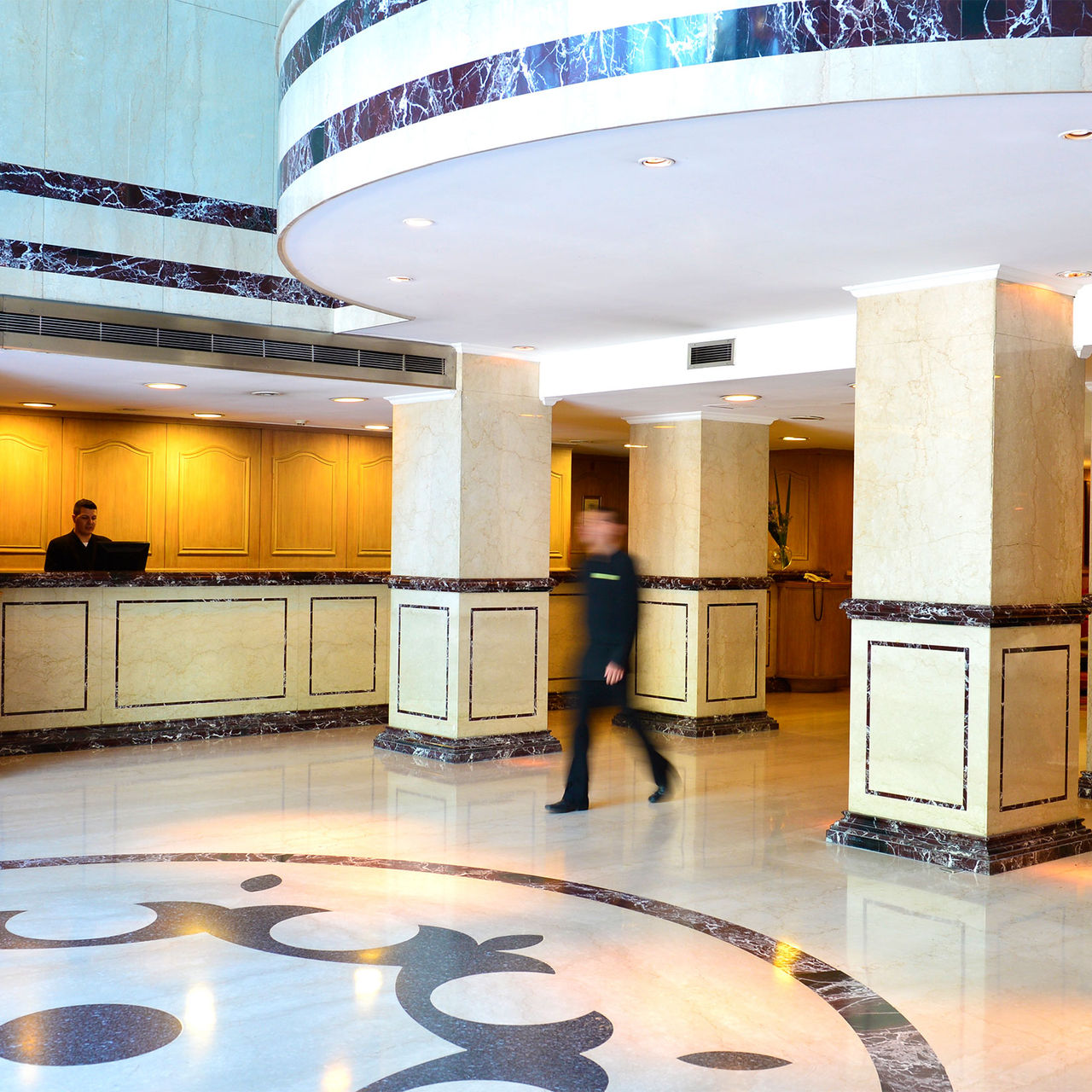Hotel entrance lobby with a person at the reception desk and another walking towards the entrance