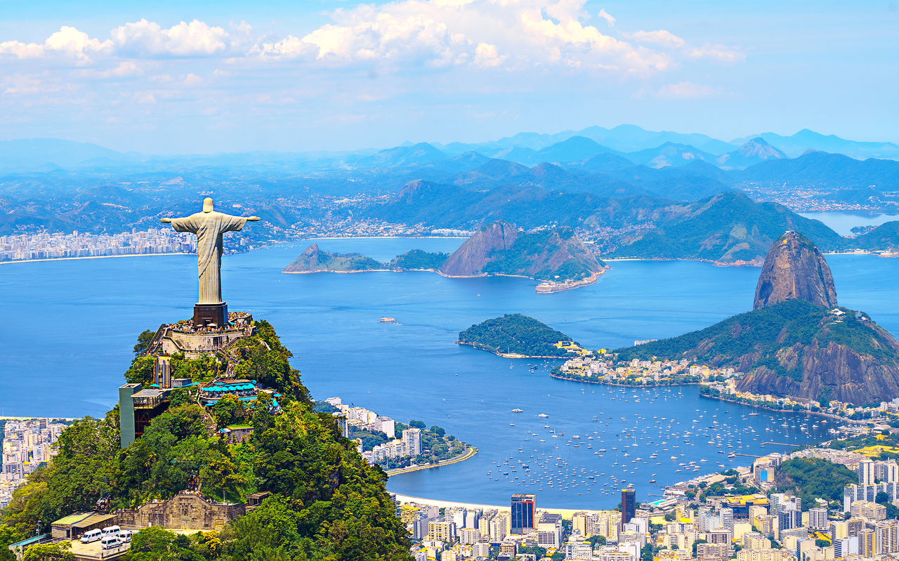 Iconic statue of Christ the Redeemer in Rio de Janeiro, with the city, ocean, and beach in the background