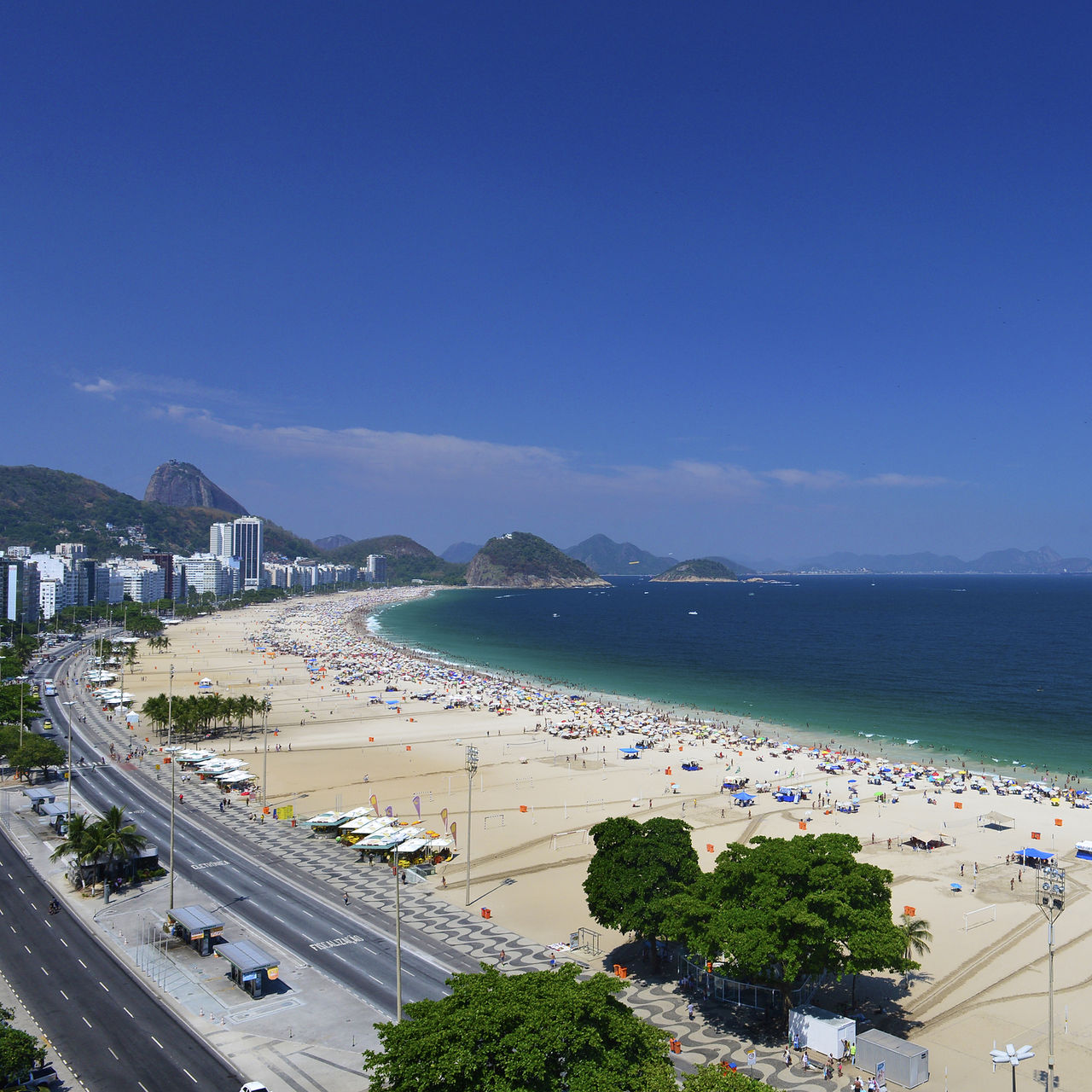 Copacabana Beach in Rio de Janeiro, a busy beach with golden sand, blue sea, and mountains in the background
