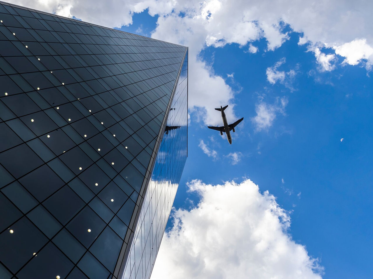 Glass facade of a building in São Paulo with reflections of clouds and a plane in flight