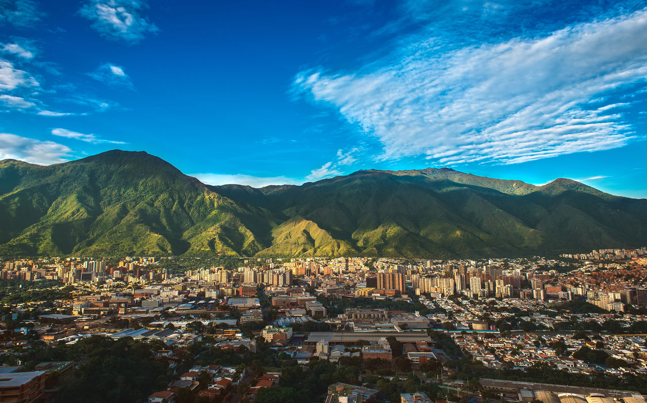 Aerial view of the city of Caracas, with tall buildings, contrasting with the mountainous nature, and the blue sky