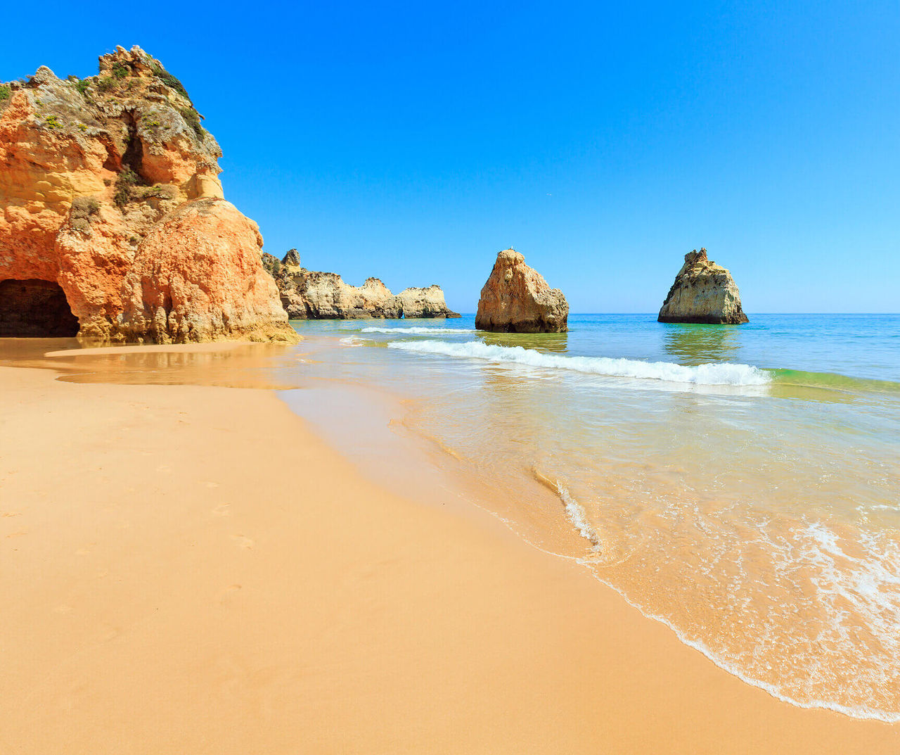 Algarve hotel overlooking golden cliffs, calm ocean waves and sandy shoreline under a clear blue sky
