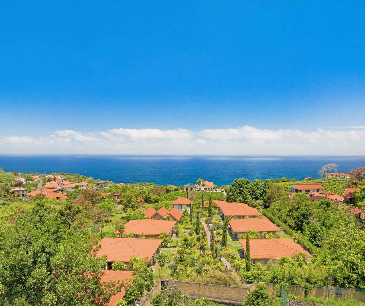 Madeira hotel overlooking terracotta roof villas surrounded by gardens with expansive ocean and blue sky