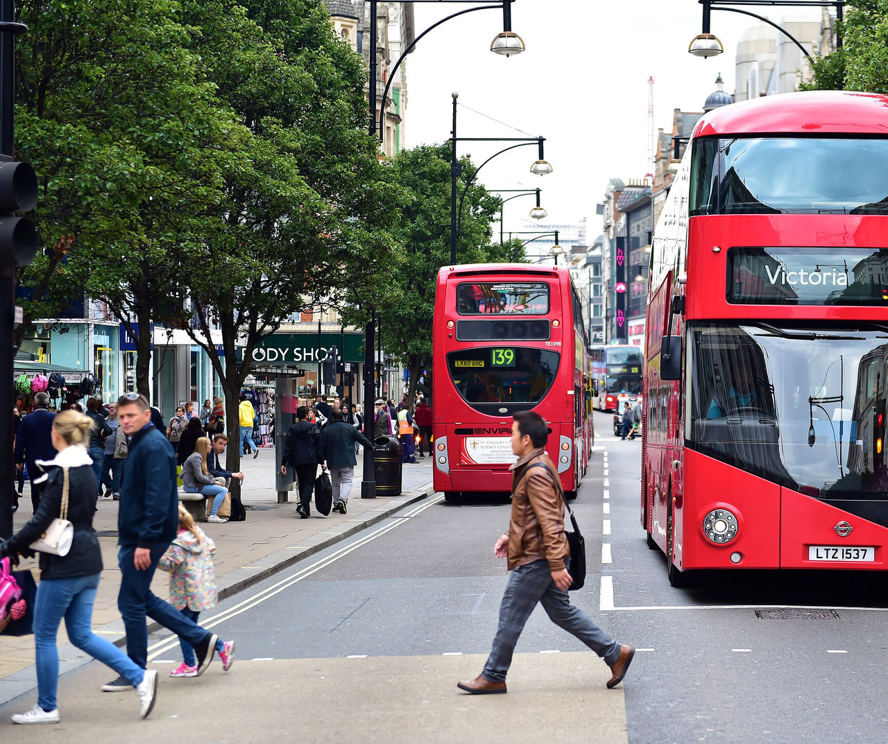 London hotel featuring red double decker buses and pedestrians crossing a busy tree lined city street
