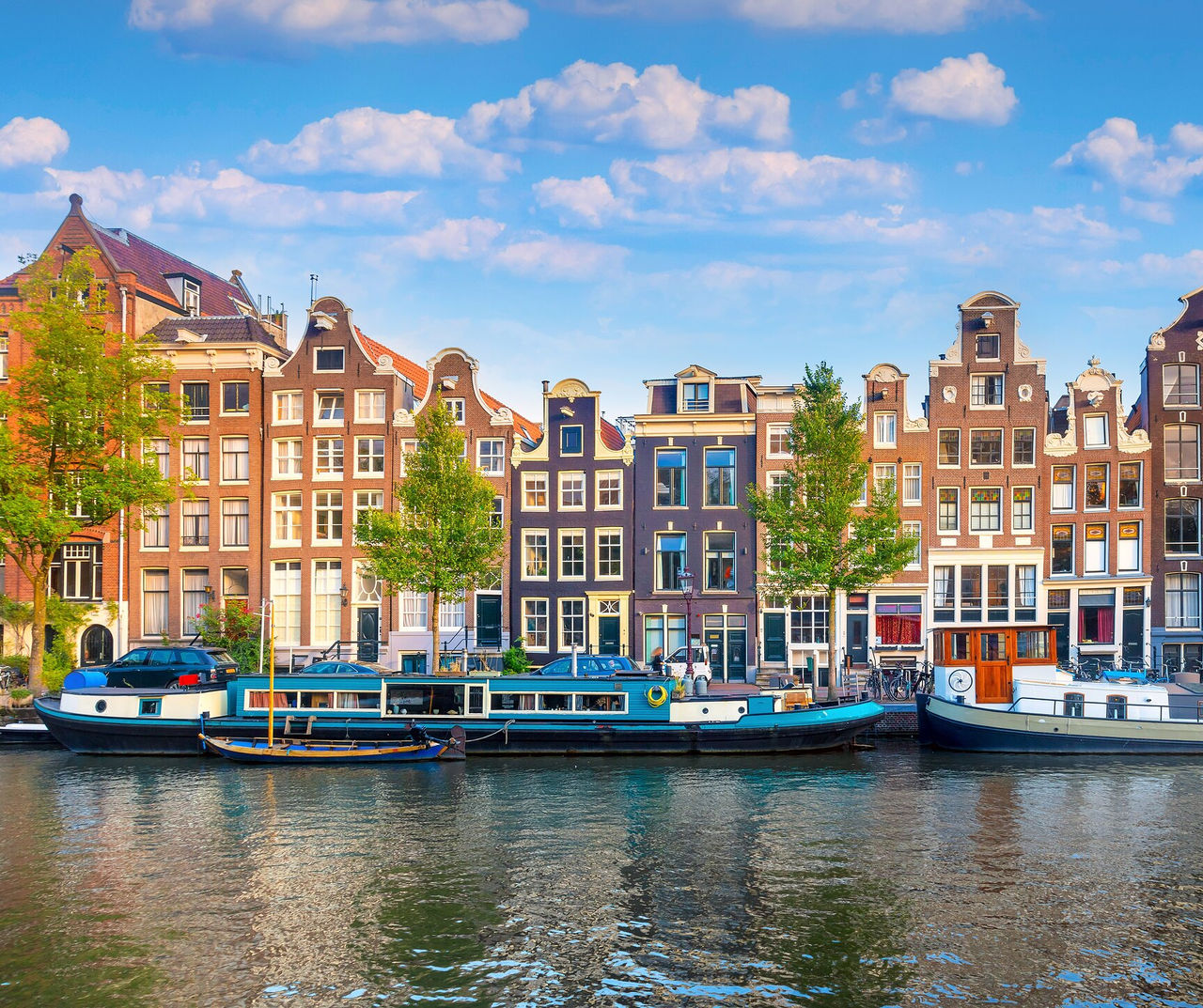 Amsterdam hotel overlooking canal boats and narrow historic houses beneath a blue sky with scattered clouds