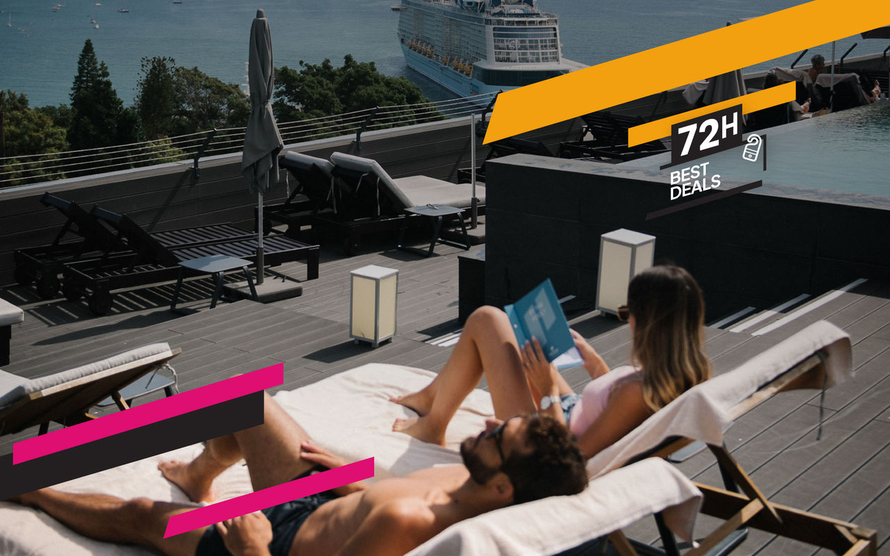 Couple relaxing on rooftop loungers beside an infinity pool overlooking the sea with a cruise ship nearby
