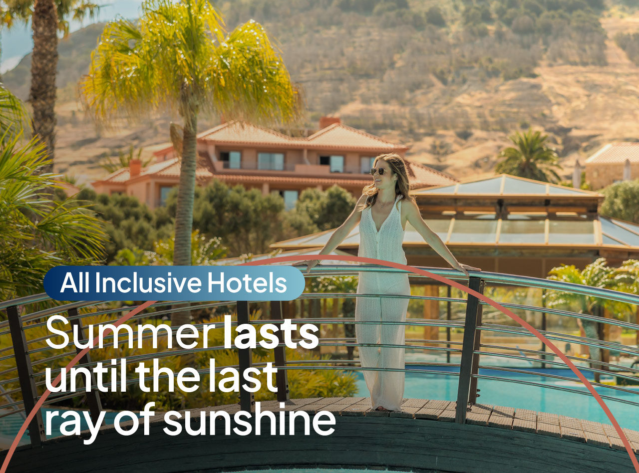 Woman standing on a curved bridge beside a resort pool with palm trees and hillside villas in warm sunlight