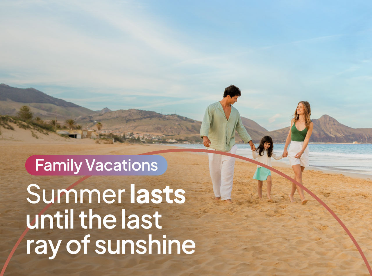 Family walking barefoot along a sandy beach at sunset with mountains and calm ocean under a clear sky