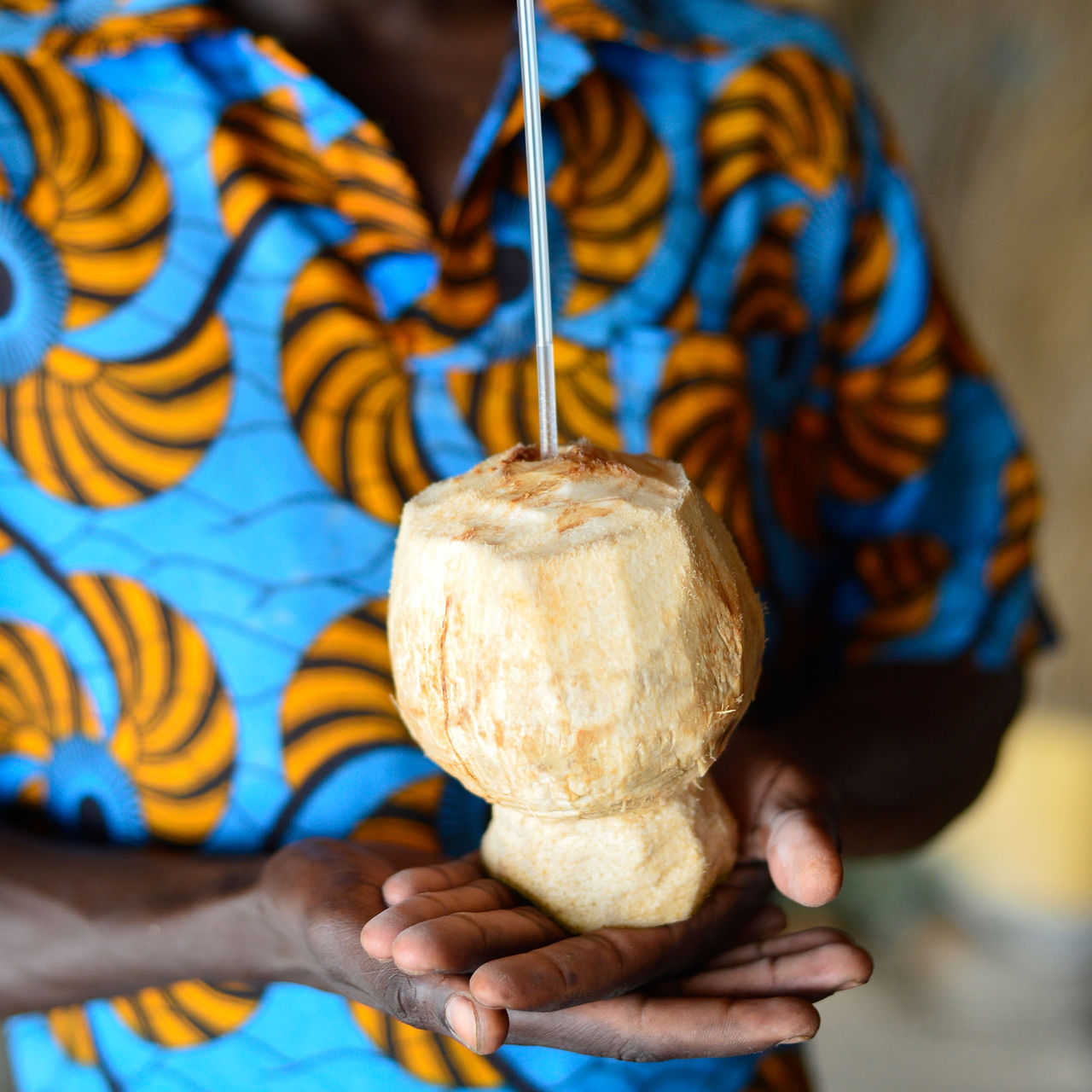 Hombre con una camisa de patrón típico y un agua de coco, en su propio coco, en la mano