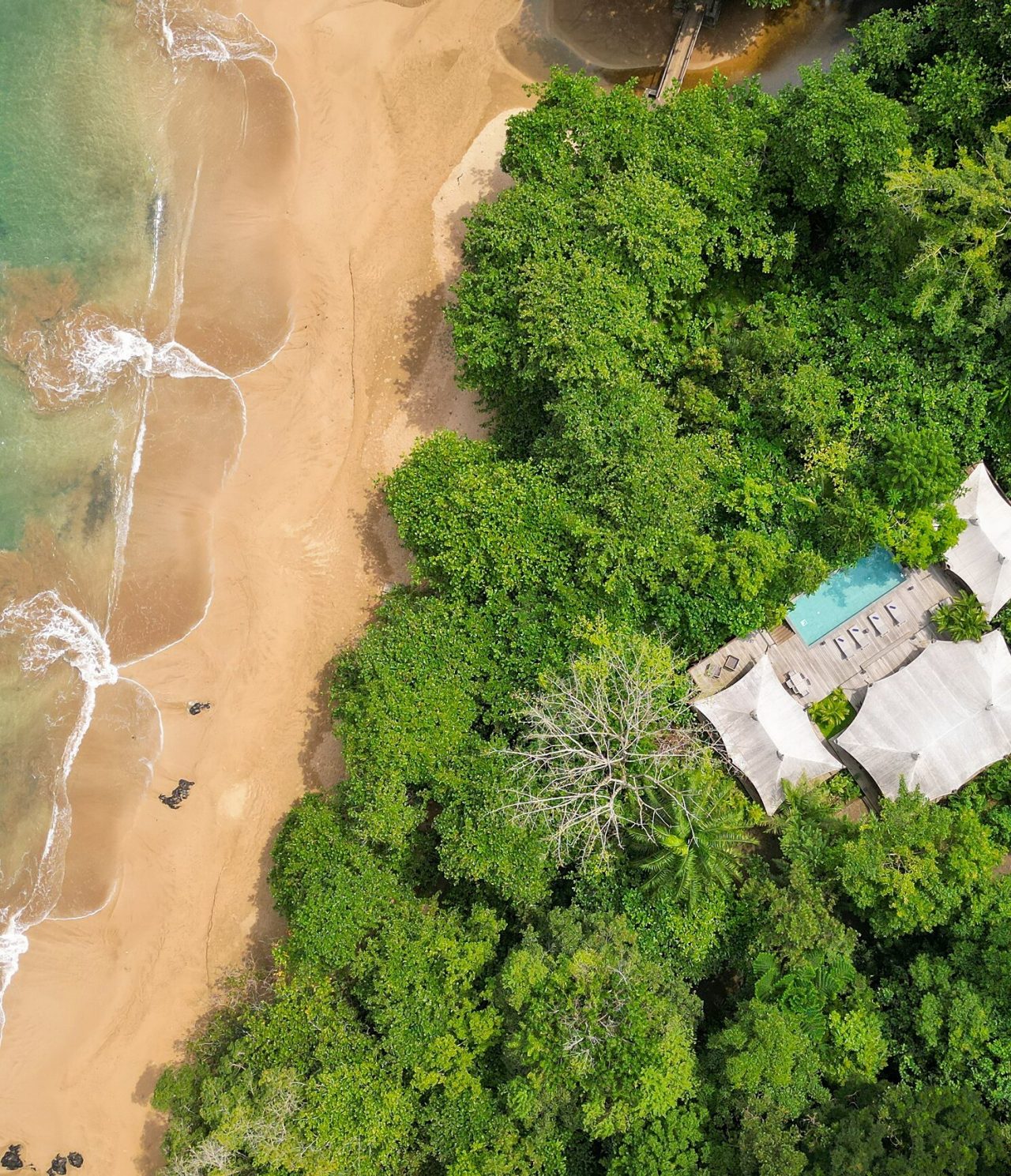 Vista aérea de la isla de São Tomé y Príncipe, edificio con piscina y una playa de arena blanca con aguas cristalinas