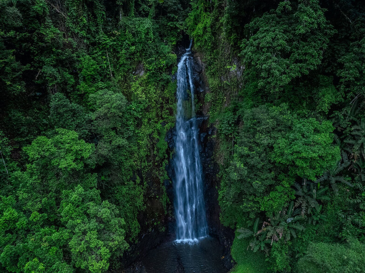 Cascada larga en medio de una vegetación densa, que desemboca en un pequeño lago en São Tomé