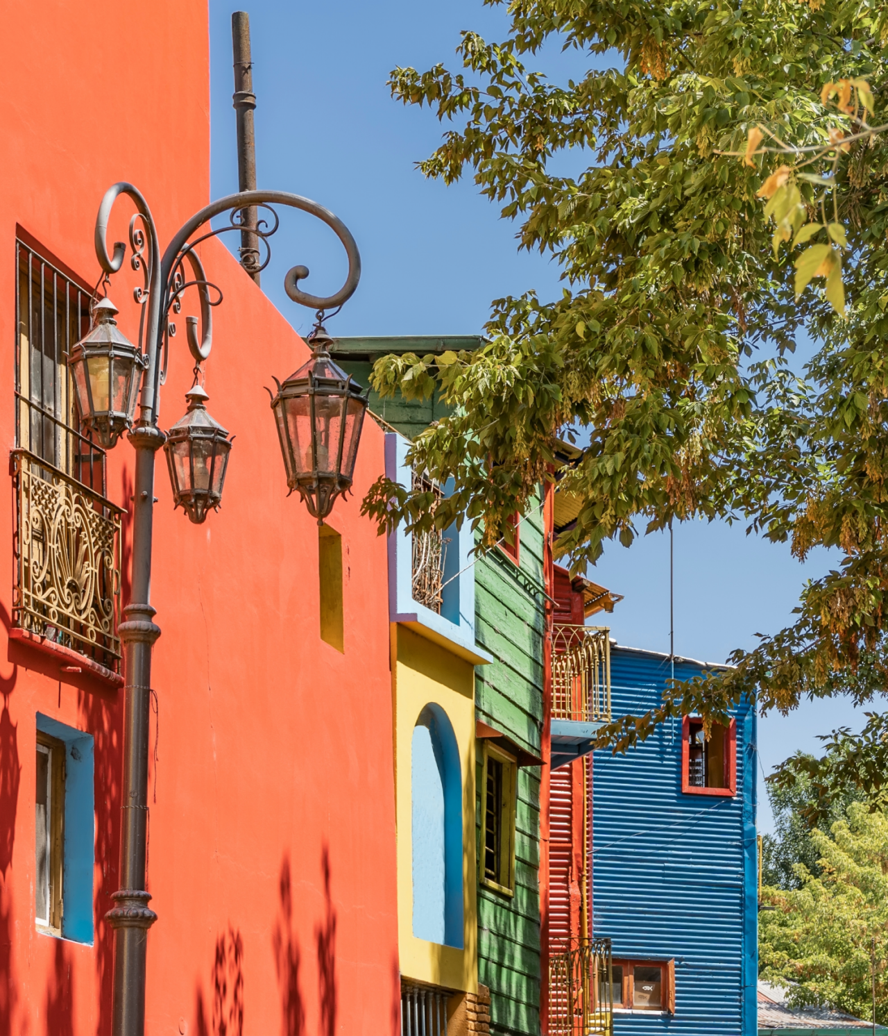 Edificios coloridos en el típico barrio Caminito de Buenos Aires, con árboles delante y un cielo azul detrás