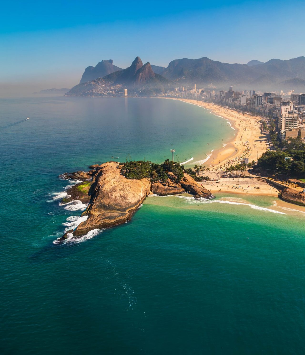 Vista aérea de Río de Janeiro, con montañas al fondo, playa de arena blanca y mar azul turquesa