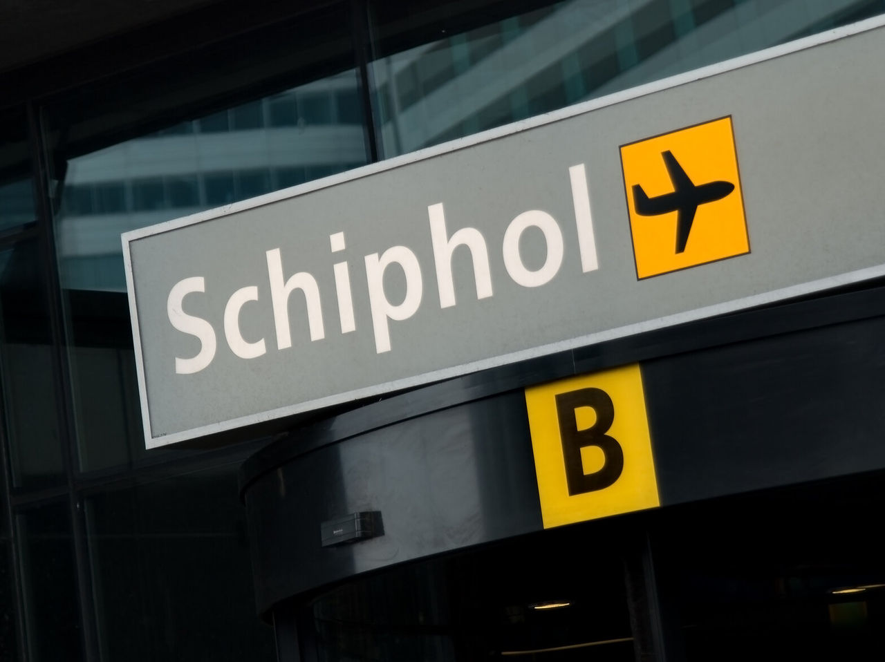 Explora Hoteles en Ámsterdam, mostrando un cartel de Schiphol con símbolo de avión junto a la entrada