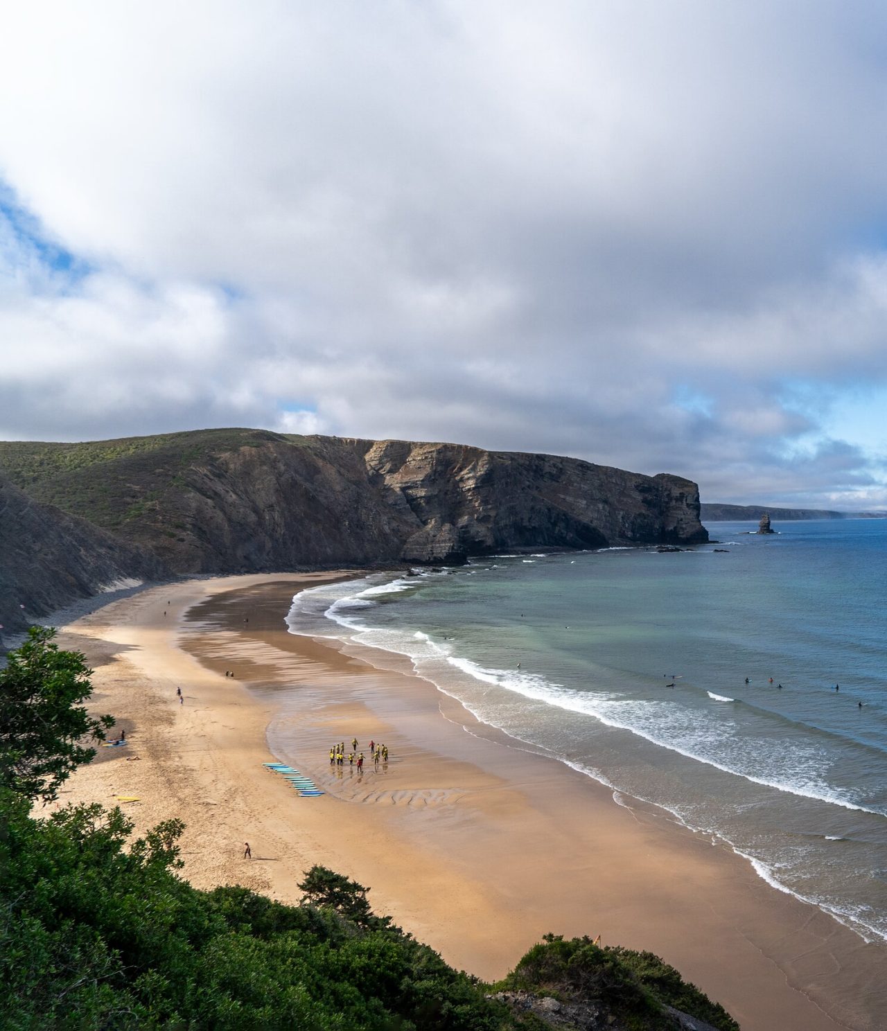 Vista panorámica de una playa extensa con acantilados rocosos y surfistas en las olas, en la región del Algarve