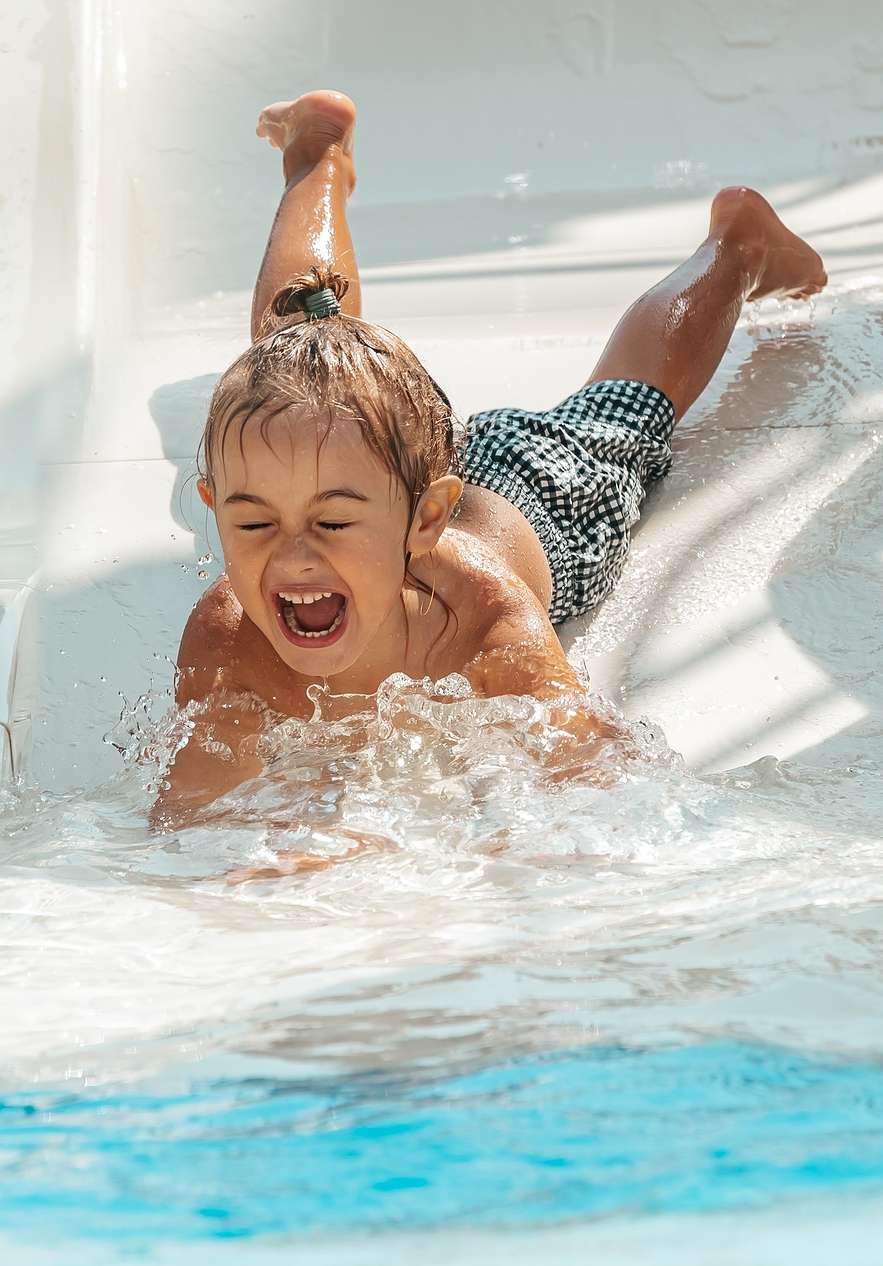 Niño sonriente deslizándose por el tobogán del parque Slide & Splash hacia la piscina