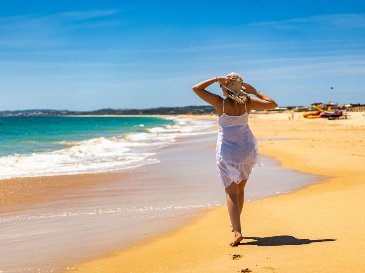 Explora Hoteles en Alvor, Algarve donde visitantes pasean por una playa dorada junto al mar azul tranquilo