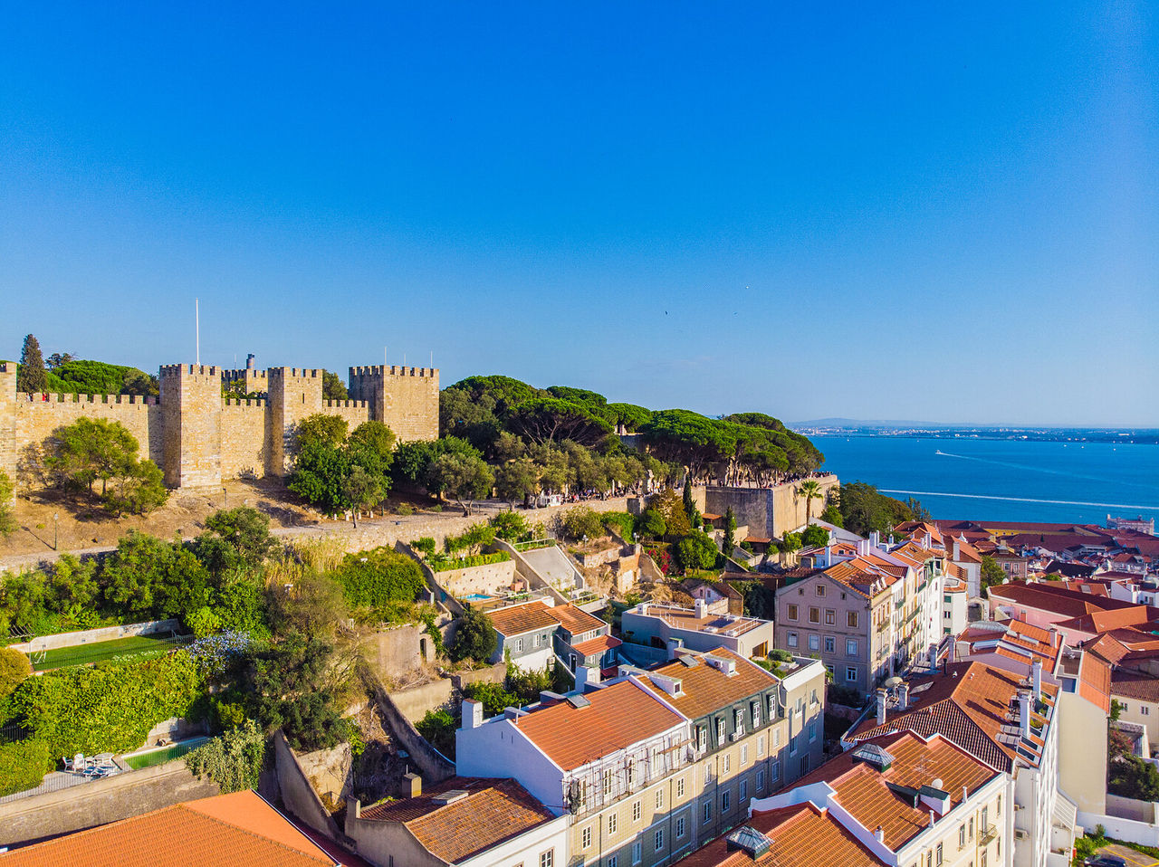 Explora Hoteles en Lisboa con vistas a las murallas históricas, tejados y el río bajo cielo despejado