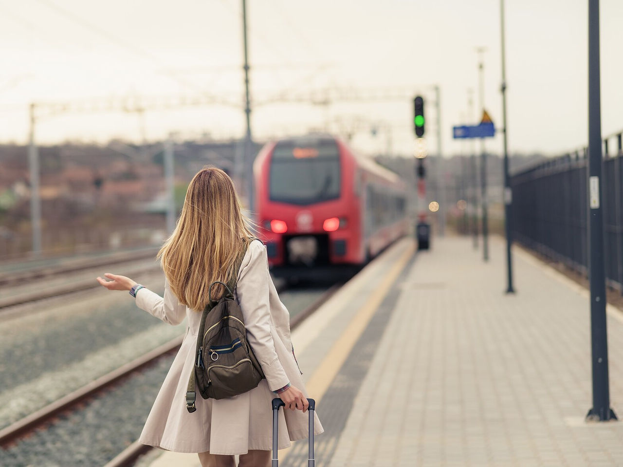 Explora Hoteles en Lisboa donde una viajera espera junto a un andén mientras llega un tren rojo al atardecer