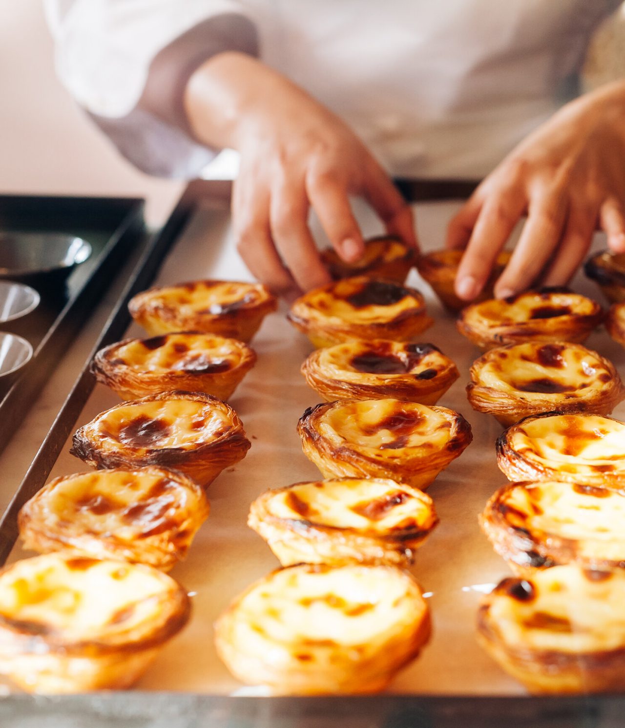 Explora Hoteles en Lisboa presentando bandejas con pasteles portugueses recién horneados en una cocina