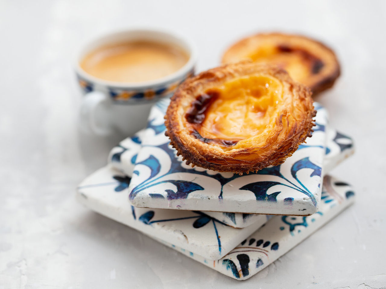 Explora Hoteles en Lisboa presentando pasteles de nata dorados junto a una taza de café sobre azulejos