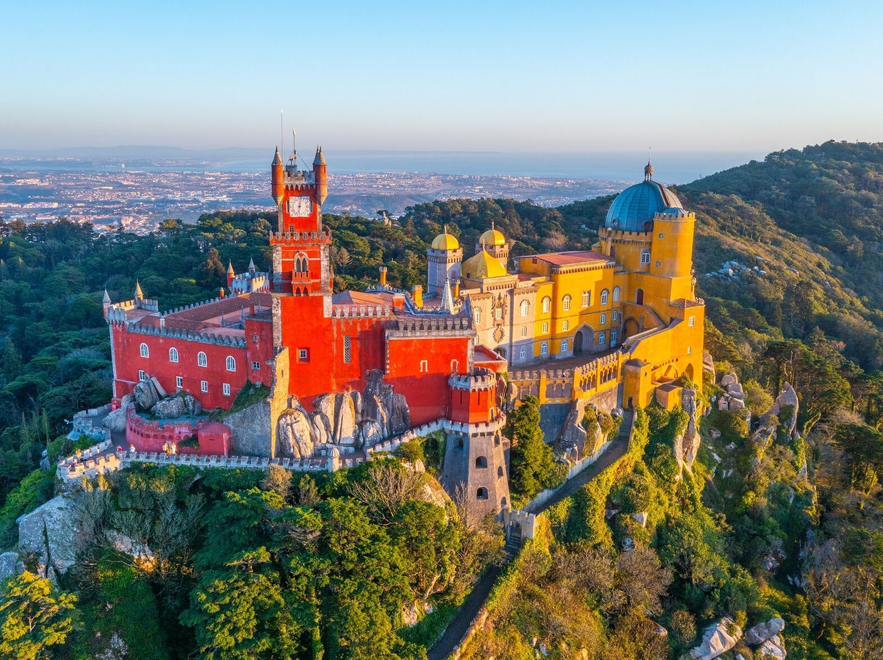 Explora Hoteles en Lisboa con vistas aéreas del colorido Palacio da Pena rodeado por colinas boscosas