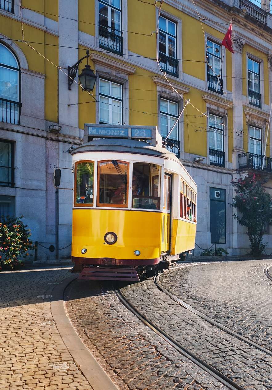 Vista frontal de un tranvía amarillo de la línea Martim Moniz, con las líneas en la carretera y edificios amarillos y rosas