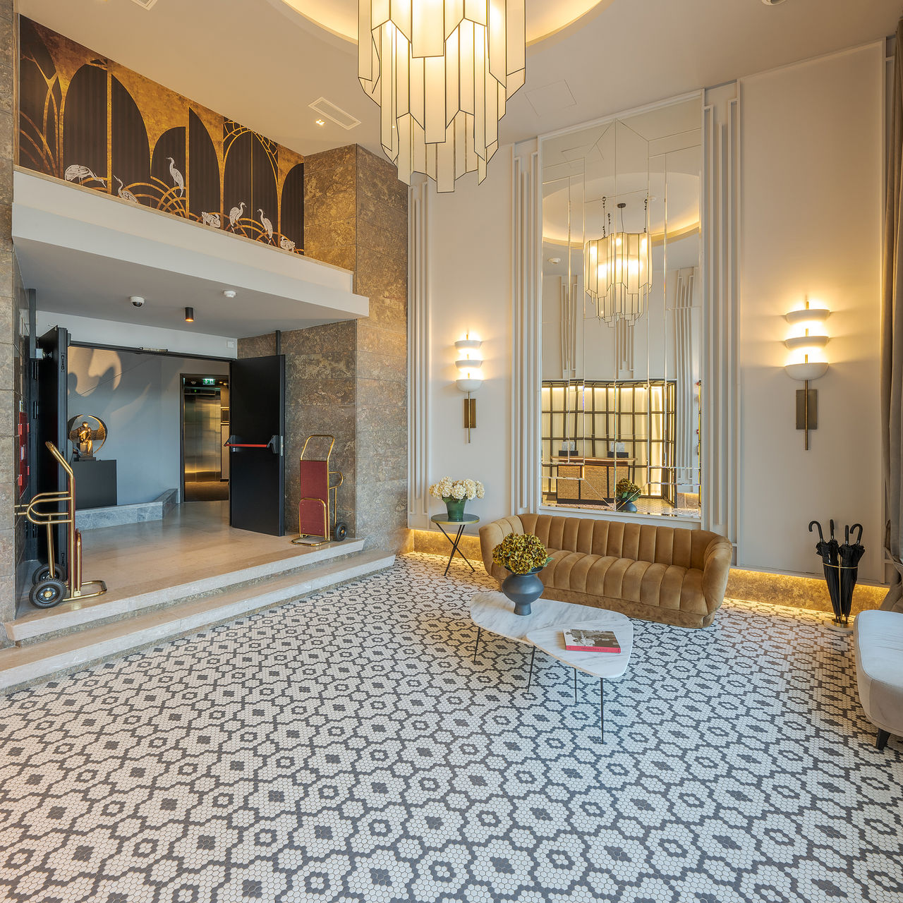 Lounge de recepción con espejos, sofás, mesas auxiliares con jarrones de flores, un candelabro y un patrón floral en el suelo