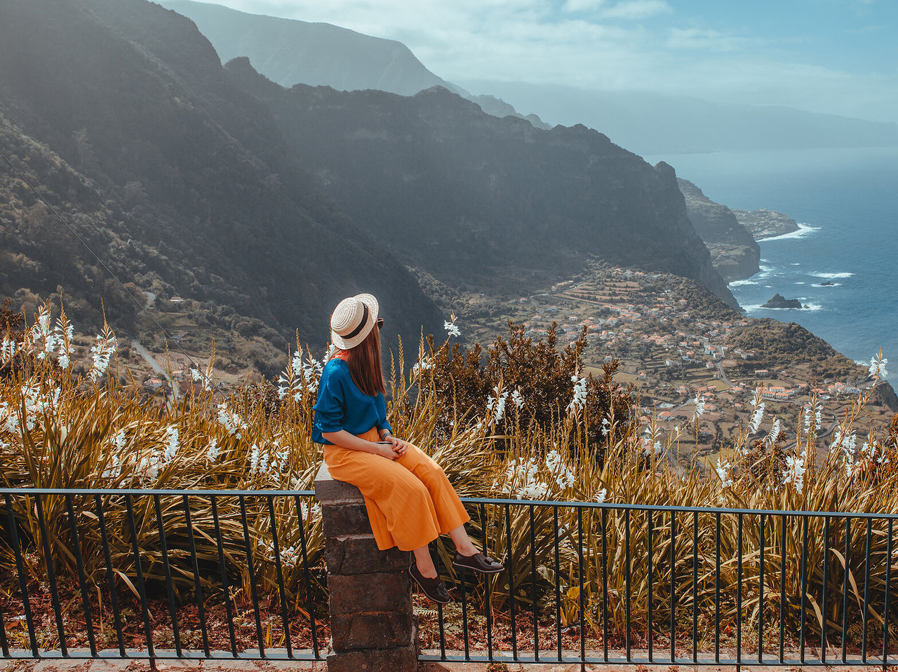 Mujer sentada en un muro disfruta de la vista de una fajã en la isla de Madeira, con el mar rodeándola