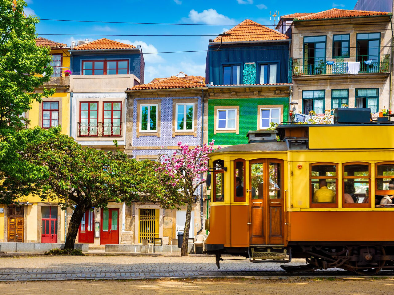 Antiguo tranvía amarillo recorriendo las estrechas calles de Oporto, pasando por casas tradicionales y encantadoras