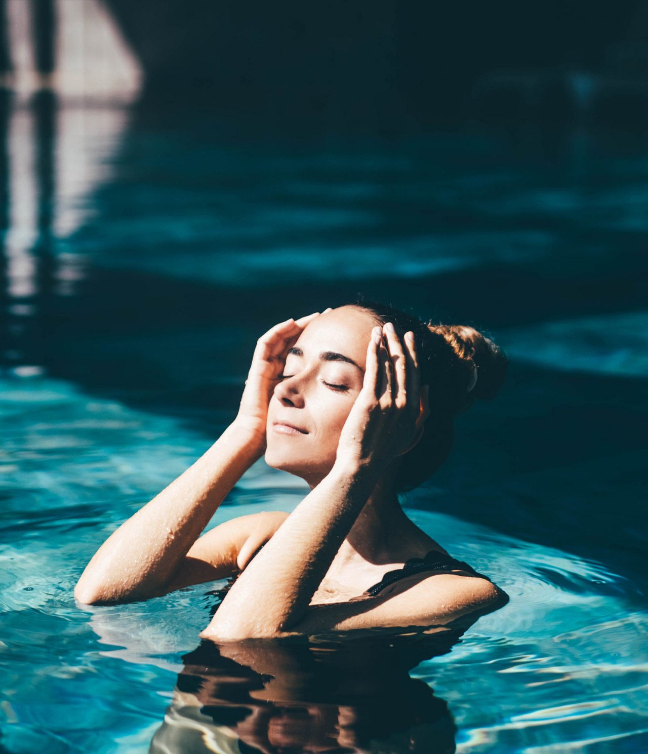 Mujer relajándose en una piscina interior iluminada suavemente mientras el agua refleja tonos azules oscuros