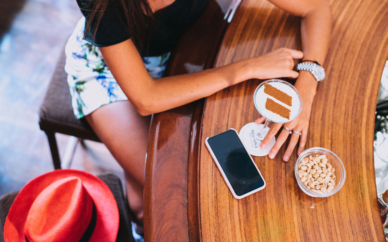Personne assise à une table en bois avec téléphone, boisson mousseuse et bol de noix vues du dessus