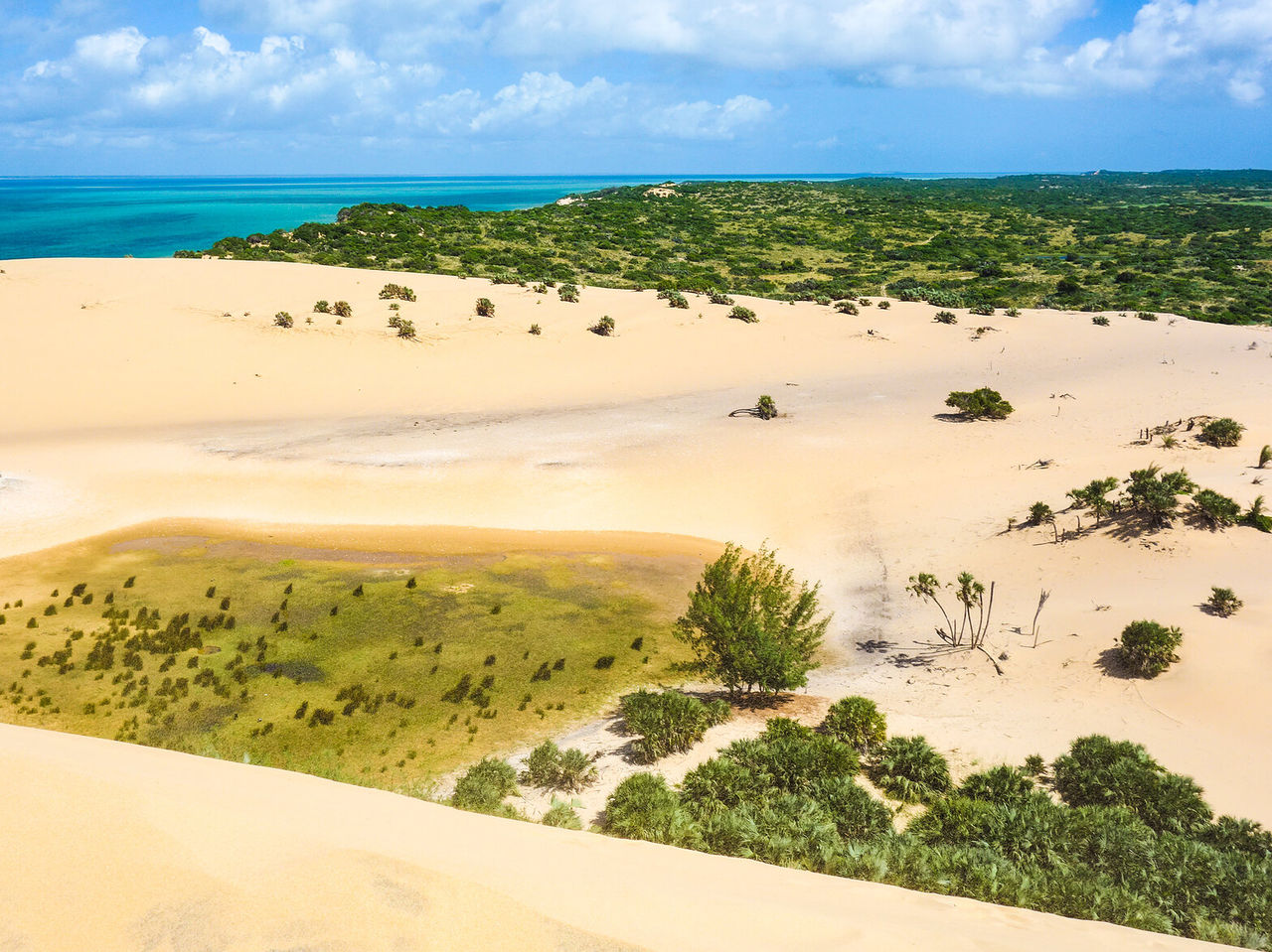 Vue aérienne d'un paysage désertique avec des dunes de sable blanc contrastant avec les eaux cristallines de l'océan